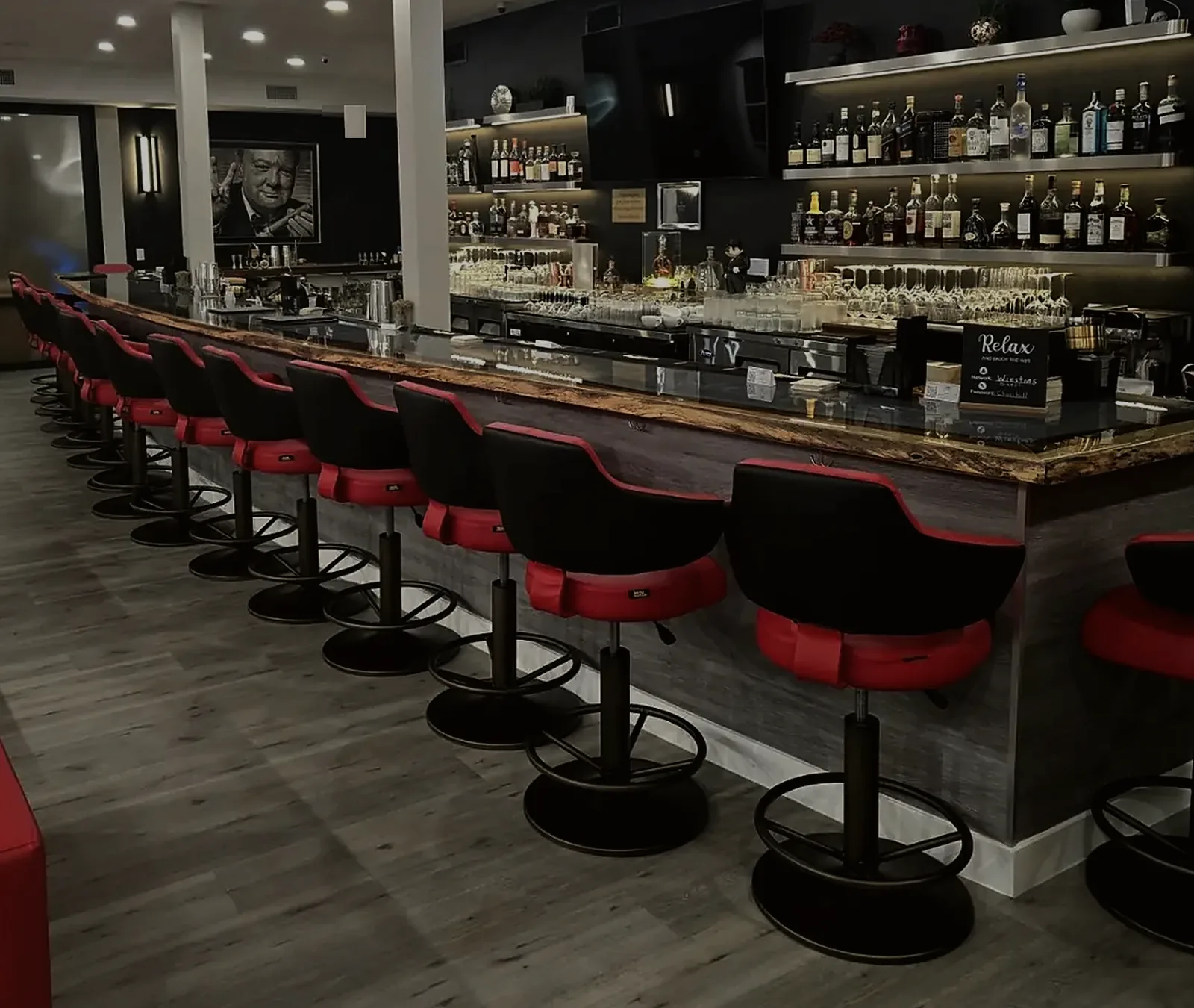 The big beautiful bar: red and black stools along a live-edge counter, the back bar lit behind it