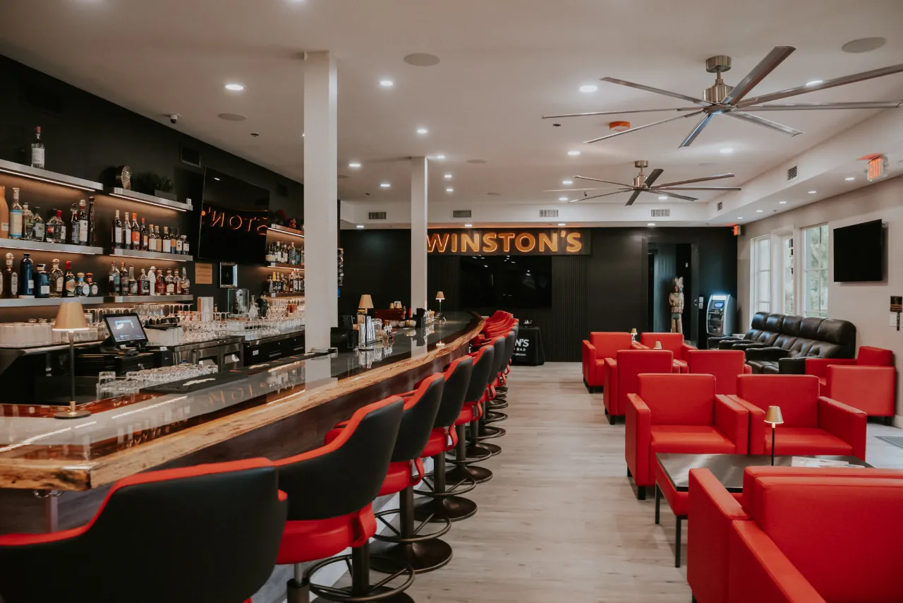The Winston's Room: a long live-edge bar with red and black stools, red leather lounge chairs and the Winston's sign